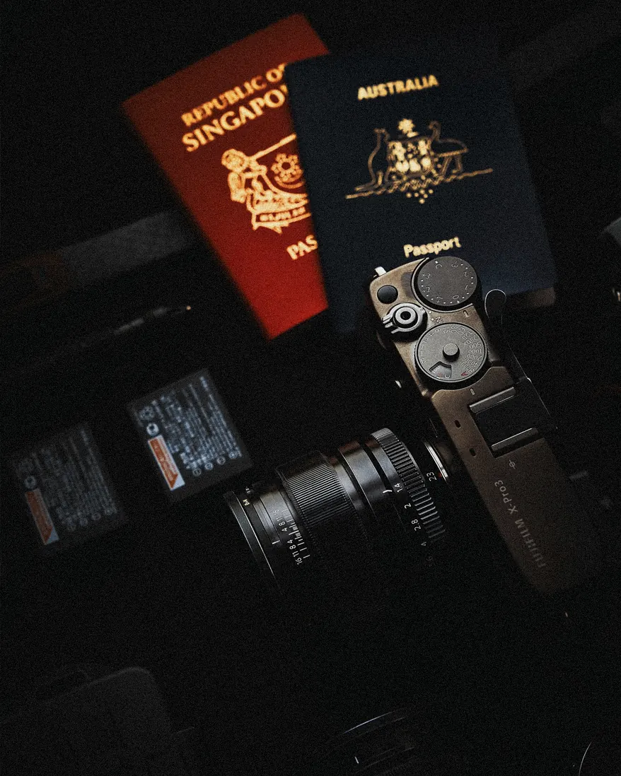 Singapore and Australian passports beside a Fujifilm X-Pro3 in low light